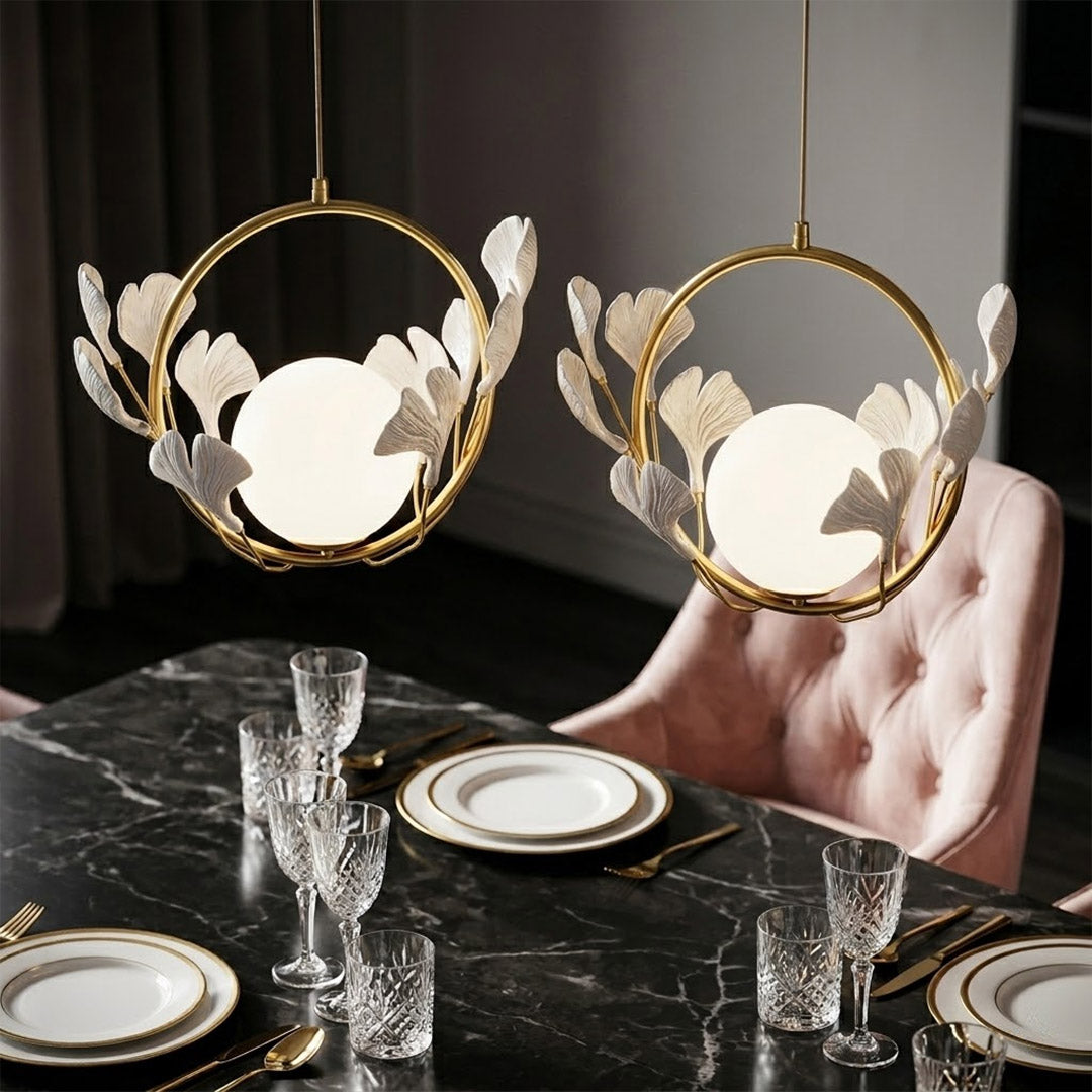 Ginkgo botanical pendant hanging above oval dining table Japandi interior warm glow porcelain leaves brass halo