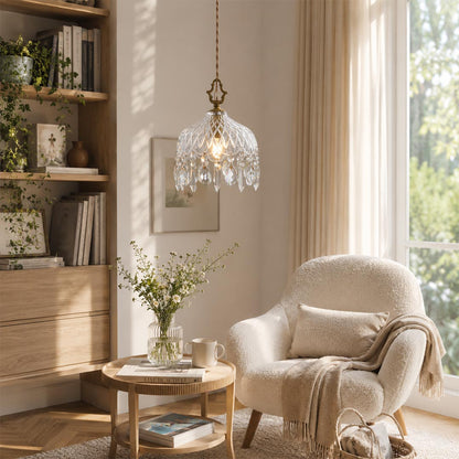 Goldie vintage brass pendant light with a clear ribbed glass bowl shade and hanging crystals, styled in a cozy neutral living room next to a white boucle armchair.
