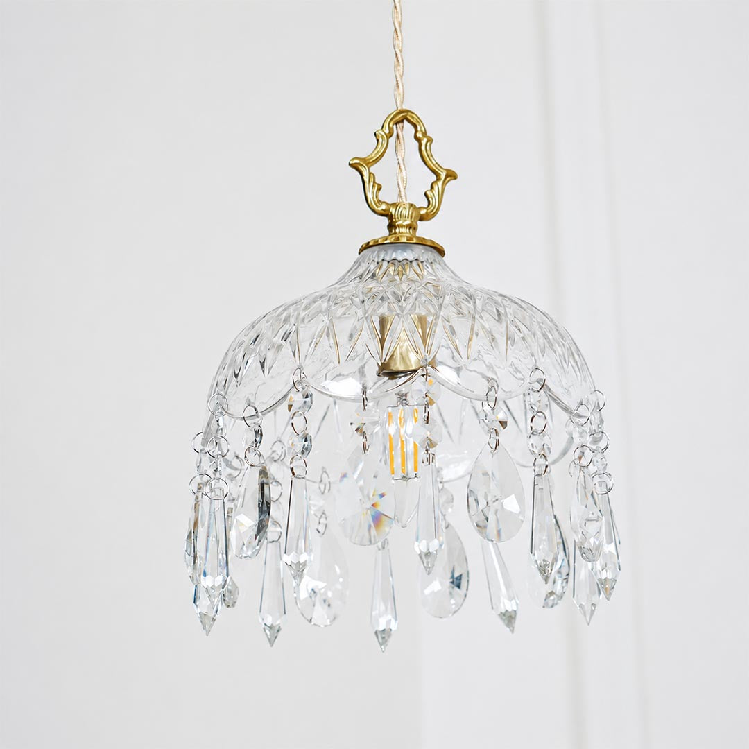 Close-up detail of Goldie vintage brass pendant light featuring an ornate brass hanger, textured cut glass bowl shade, and sparkling hanging crystal droplets with a glowing warm bulb.