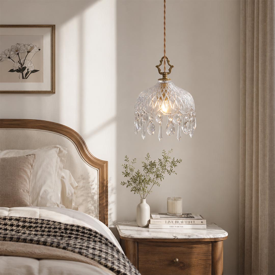 Goldie brass crystal pendant light hanging as a cozy bedroom bedside lamp above a wooden nightstand, styled in a French country aesthetic bedroom with a neutral headboard.