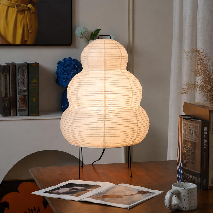 Illuminated gourd shape washi paper table lamp giving a soft warm glow on a wooden desk near books