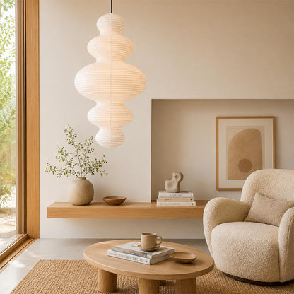 Multi-tier Stuber Lighting rice paper pendant light glowing in a minimalist entryway corner, cozy Wabi-Sabi interior design with a lounge chair.