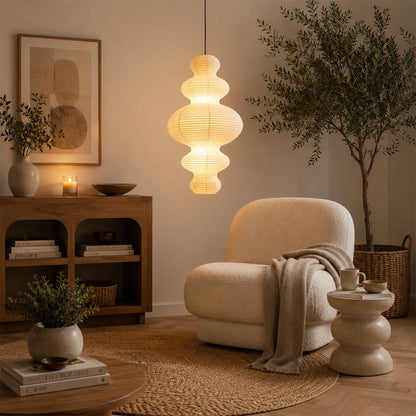 Multi-tier Stuber Lighting rice paper pendant light glowing in a minimalist entryway corner, cozy Wabi-Sabi interior design with a lounge chair.