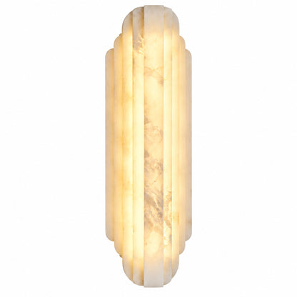 Lamina alabaster wall sconce glowing warm beside a bed in a modern bedroom