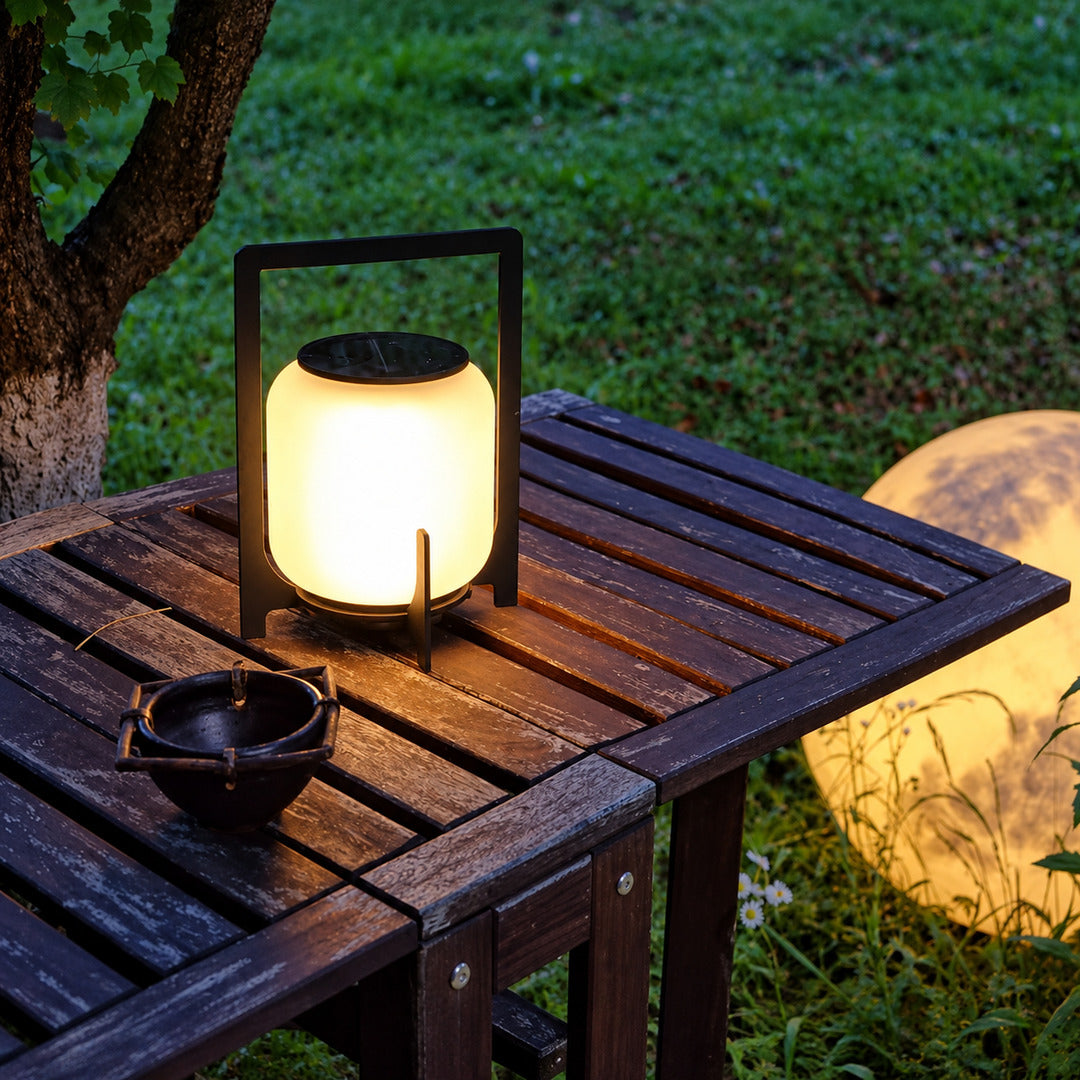 Lucciola rechargeable lantern glowing warmly on a patio dining table at dusk