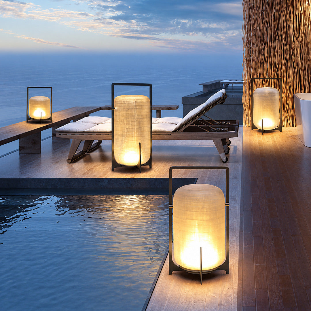 Lucciola rechargeable lantern on a poolside table casting a warm evening glow