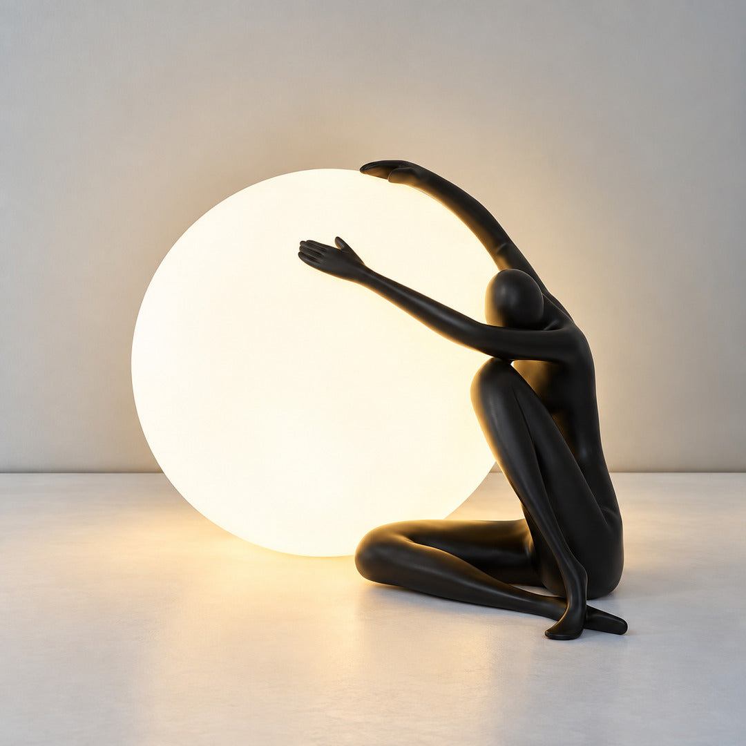 Small black Musa sculpture table lamp glowing warm on a nightstand