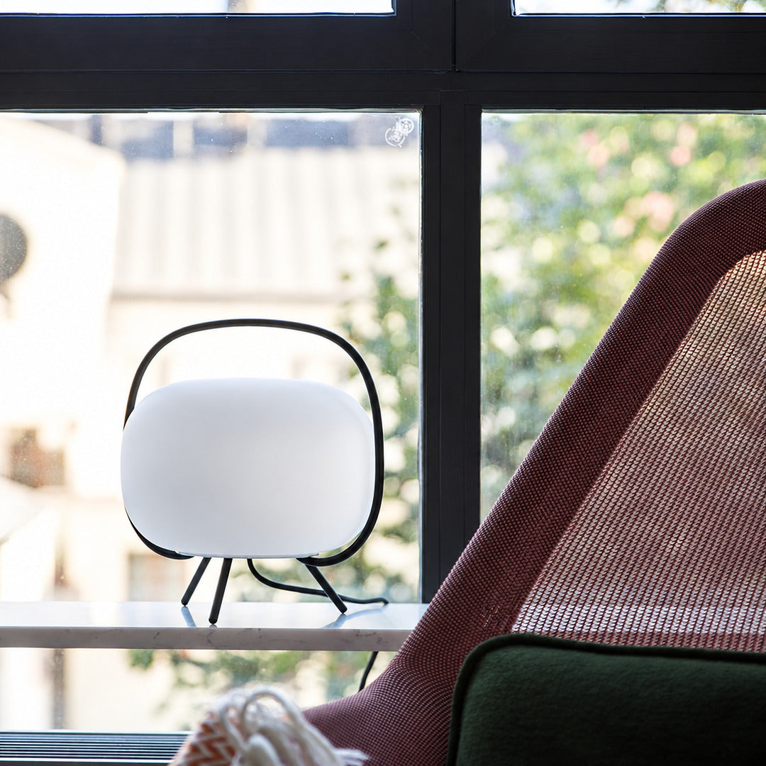 Nomade glass table lamp casting a warm glow over a corner reading chair