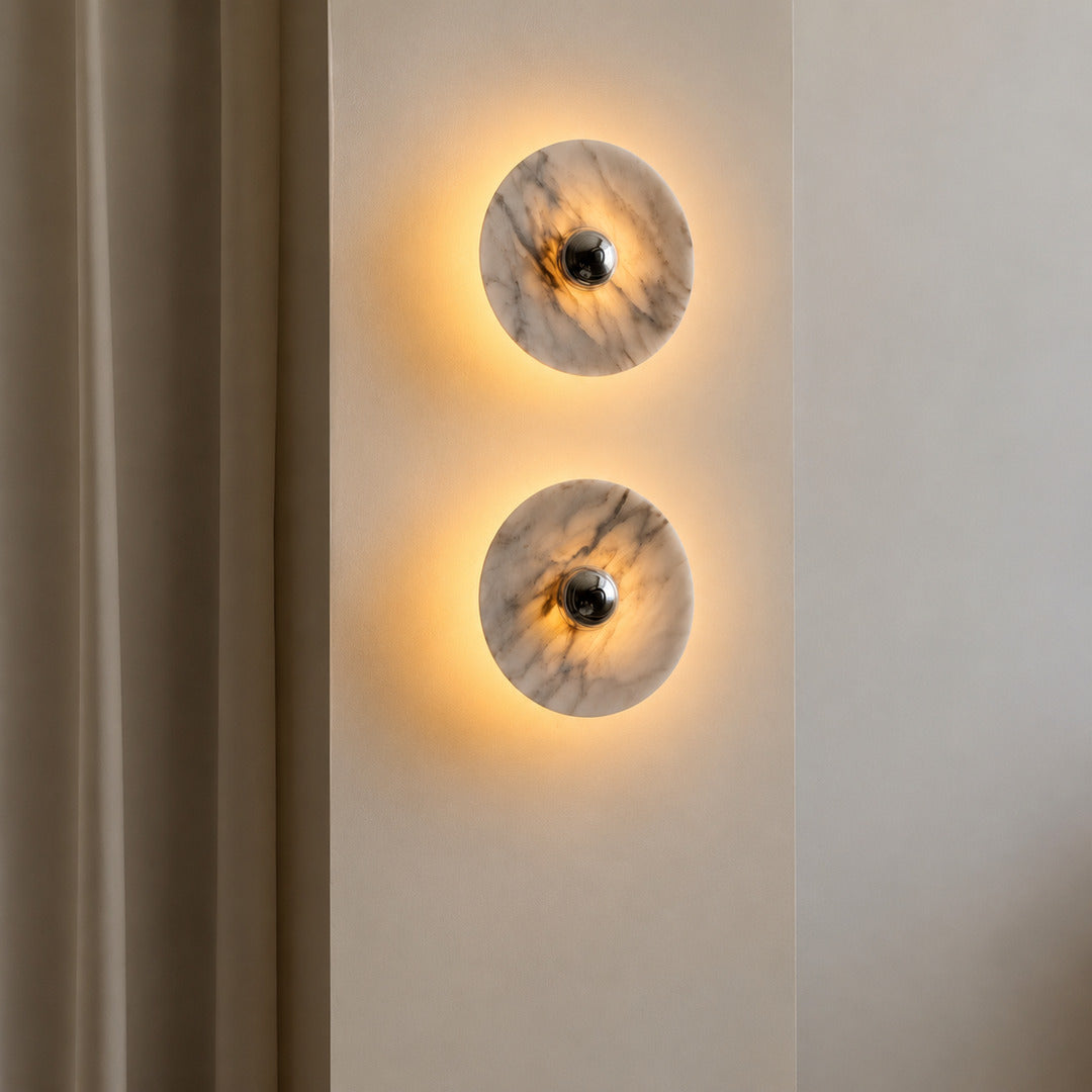Warm integrated LED glow washing softly across the natural marble face of the Orbe wall sconce