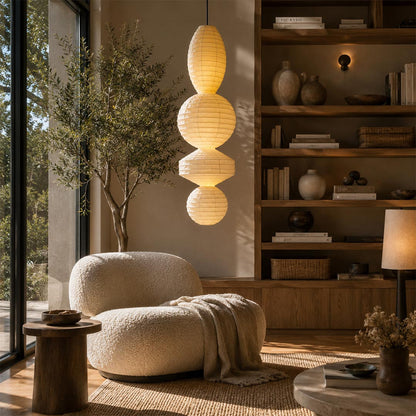 A cozy Japandi lounge chair corner illuminated by a stacked orb Ori Lantern Series Pendant Light by Stuber Lighting.