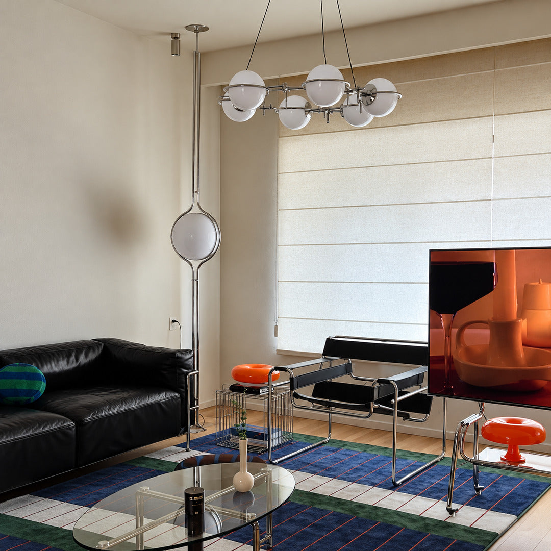 Pendolo floor to ceiling lamp glowing in the corner beside a leather sofa in a mid-century living room
