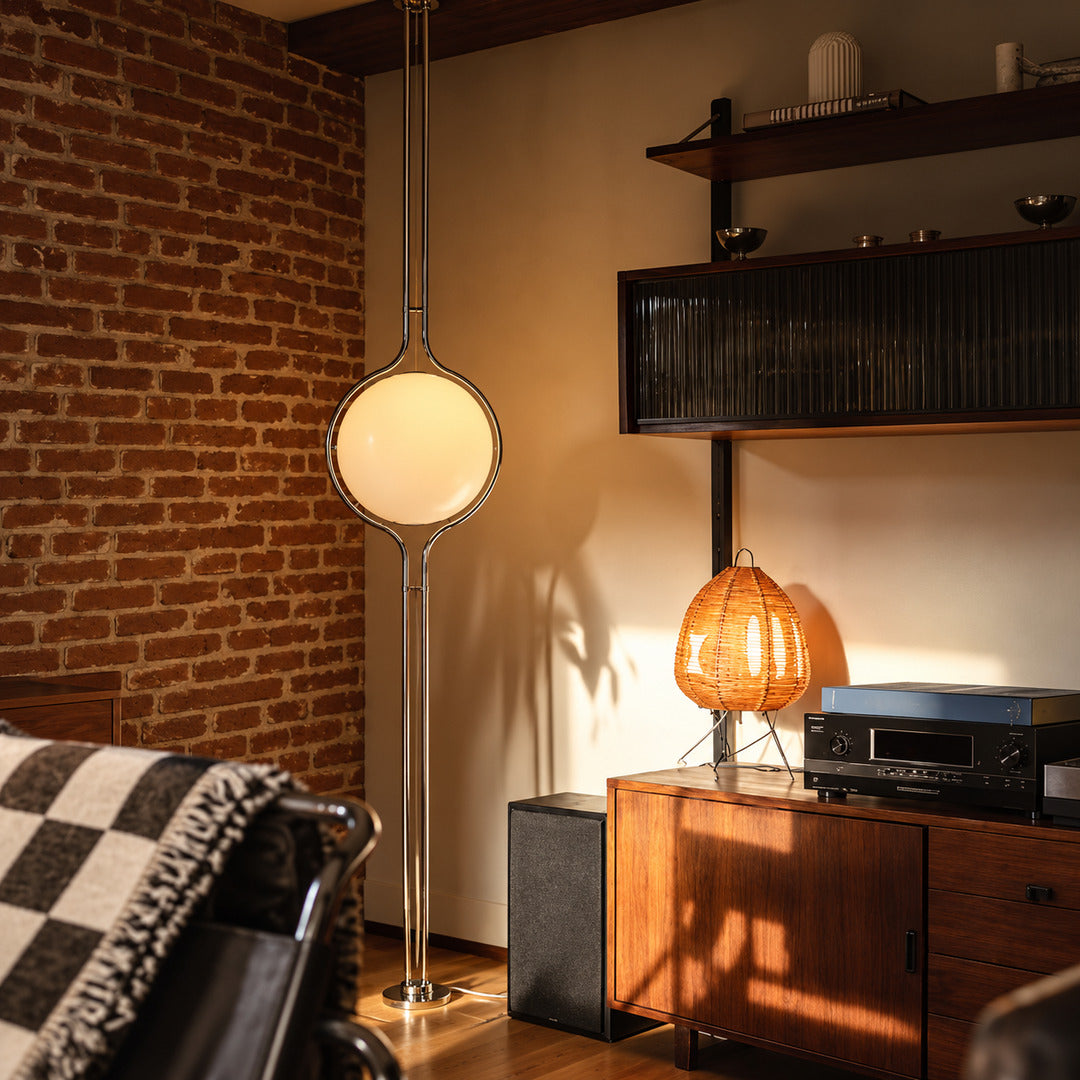 Pendolo floor to ceiling lamp glowing in the corner beside a leather sofa in a mid-century living room