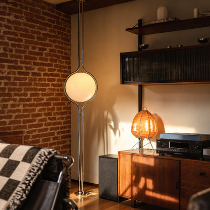 Pendolo floor to ceiling lamp glowing in the corner beside a leather sofa in a mid-century living room