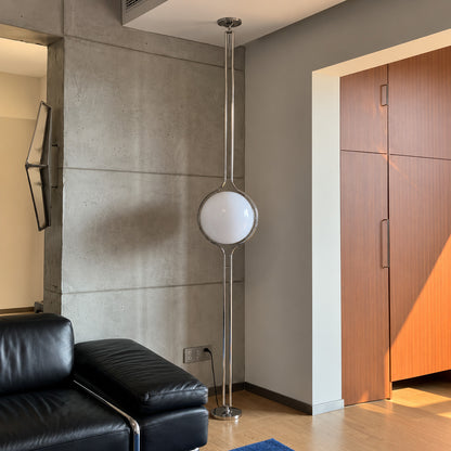 Pendolo floor to ceiling lamp glowing in the corner beside a leather sofa in a mid-century living room