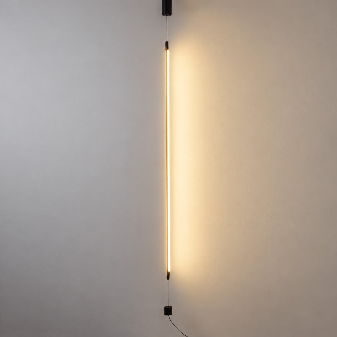 Riga floor to ceiling lamp with a slim black LED tube glowing warm in a modern living room corner