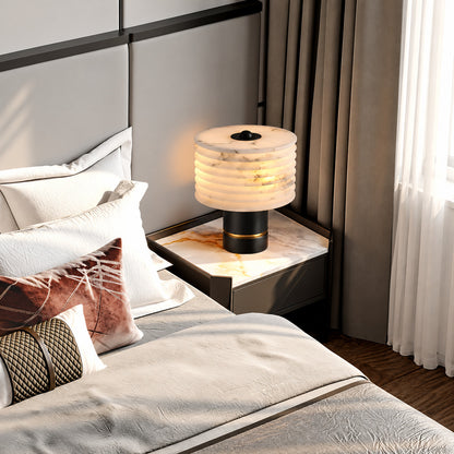 Sasso alabaster table lamp casting a soft glow on a bedside table