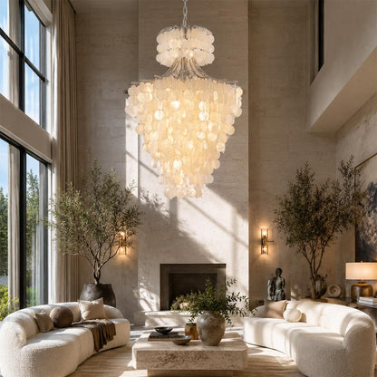 Organic modern chandelier hanging in a bright luxury living room with white sofas and a fireplace.