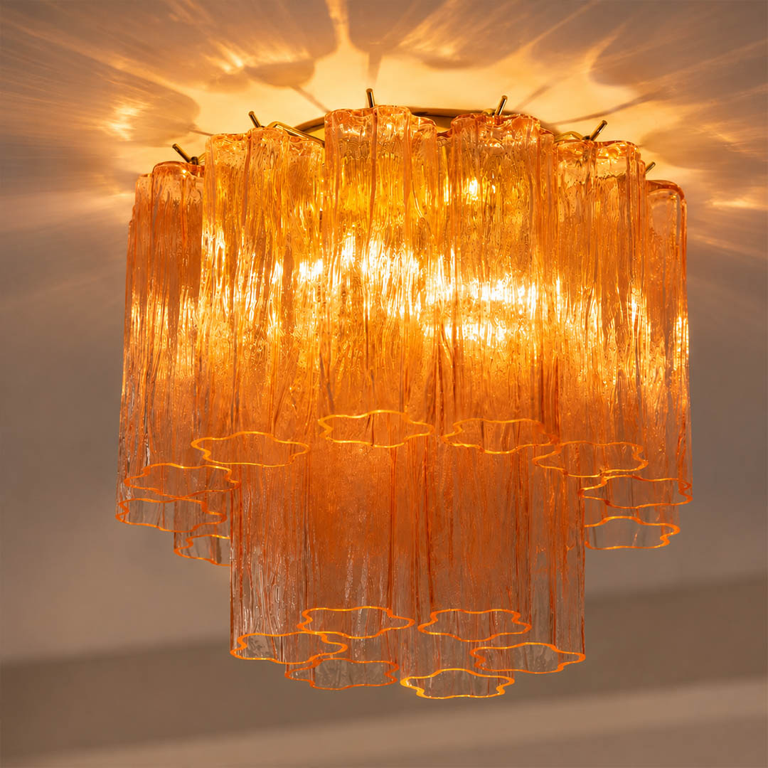 Pure white background, exact Stellina ceiling light switched on with soft warm-white light. Preserve the original glass color, texture, polished gold frame, and structure without exaggerated glow.