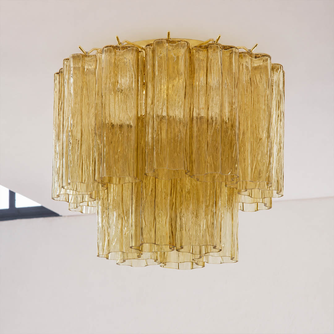Pure white background, exact Stellina ceiling light with translucent amber-gold glass and polished gold frame. Light off, centered three-quarter view, realistic refraction and restrained highlights.
