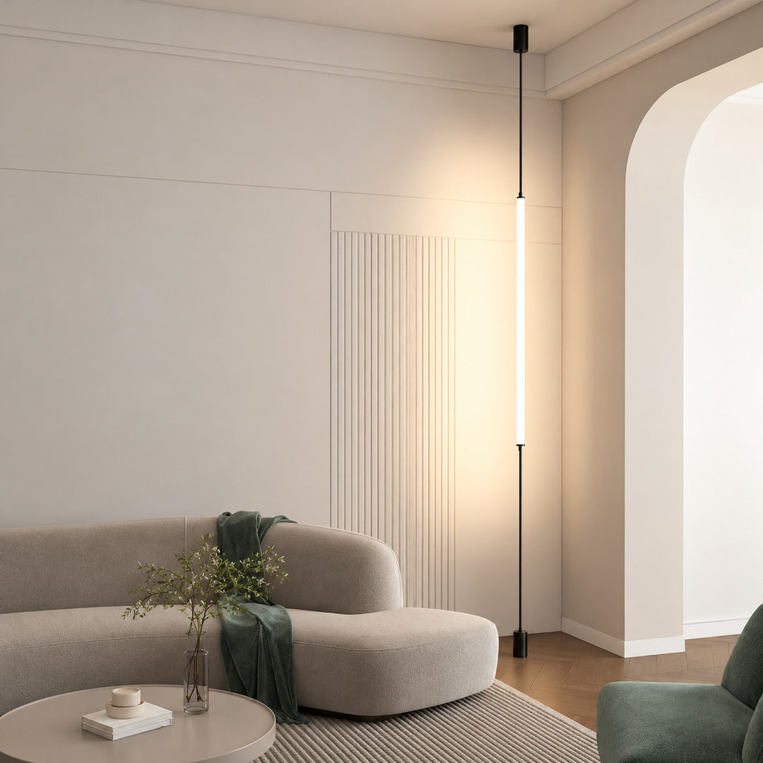 Stelo floor to ceiling lamp drawing a warm vertical line behind a low sectional sofa