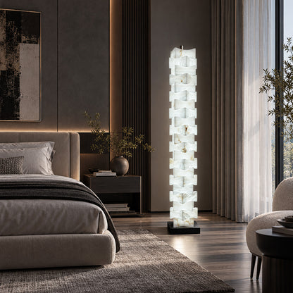 Strato stacked alabaster floor lamp beside a bed casting a soft warm glow