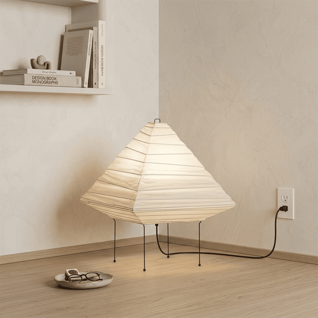 Minimalist modern home lamp: A geometric diamond-shaped washi paper table lamp with a tripod base, emitting a warm glow for cozy interior decoration lighting on a wooden desk.