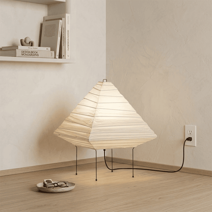 Minimalist modern home lamp: A geometric diamond-shaped washi paper table lamp with a tripod base, emitting a warm glow for cozy interior decoration lighting on a wooden desk.