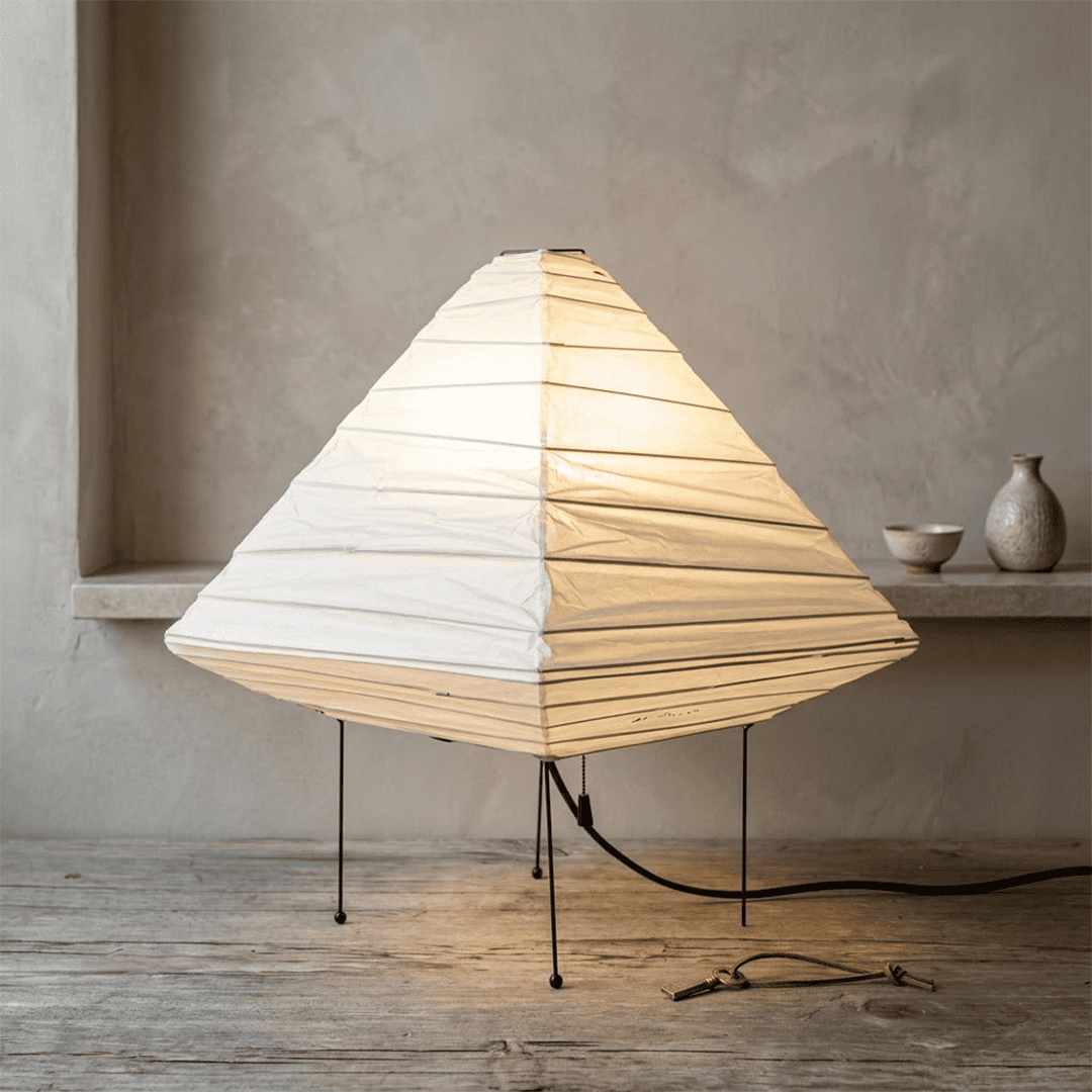 Minimalist modern home lamp: A geometric diamond-shaped washi paper table lamp with a tripod base, emitting a warm glow for cozy interior decoration lighting on a wooden desk.