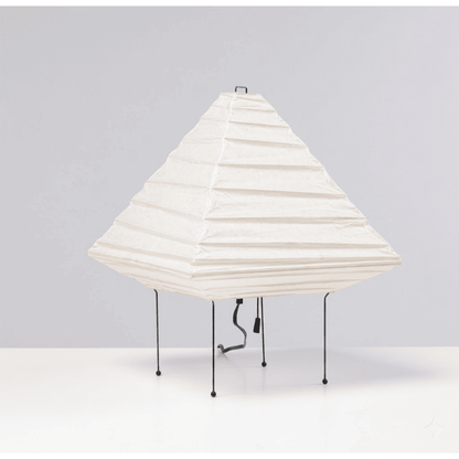 Minimalist modern home lamp: A geometric diamond-shaped washi paper table lamp with a tripod base, emitting a warm glow for cozy interior decoration lighting on a wooden desk.
