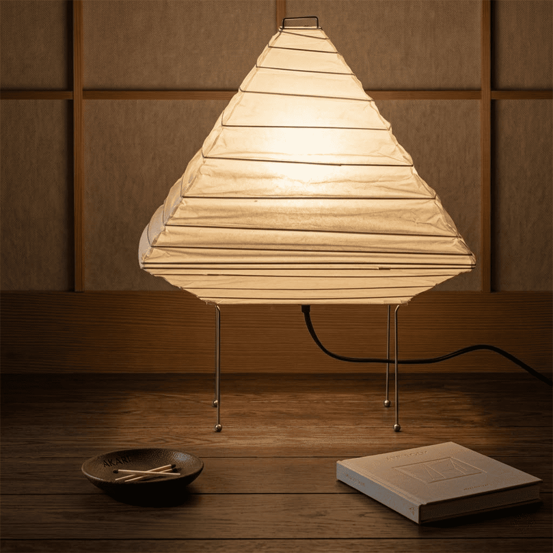 Minimalist modern home lamp: A geometric diamond-shaped washi paper table lamp with a tripod base, emitting a warm glow for cozy interior decoration lighting on a wooden desk.