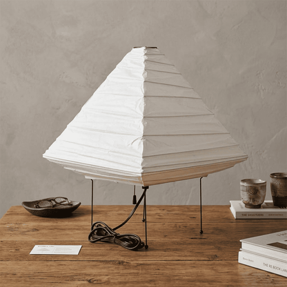 Minimalist modern home lamp: A geometric diamond-shaped washi paper table lamp with a tripod base, emitting a warm glow for cozy interior decoration lighting on a wooden desk.