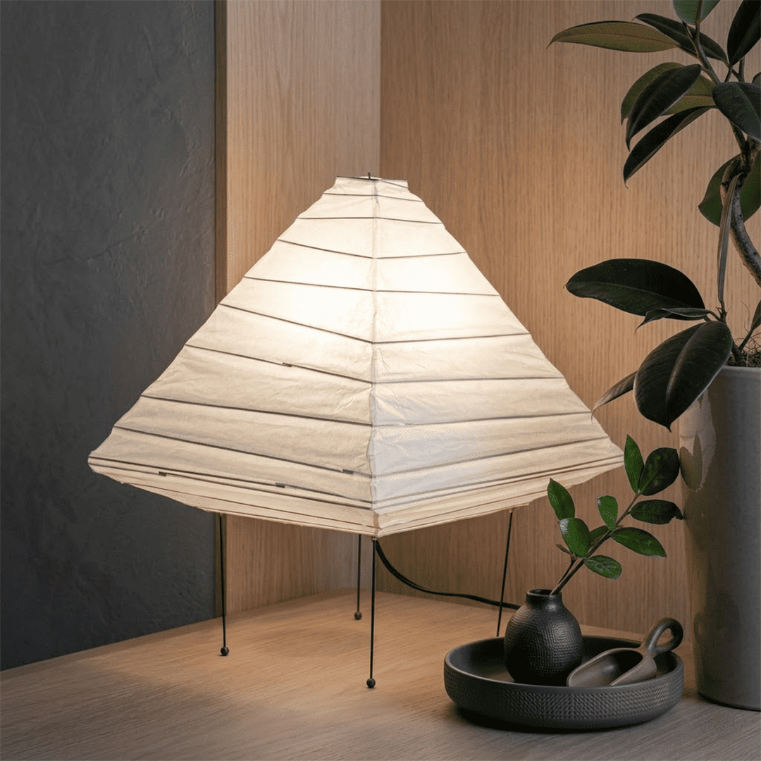 Minimalist modern home lamp: A geometric diamond-shaped washi paper table lamp with a tripod base, emitting a warm glow for cozy interior decoration lighting on a wooden desk.