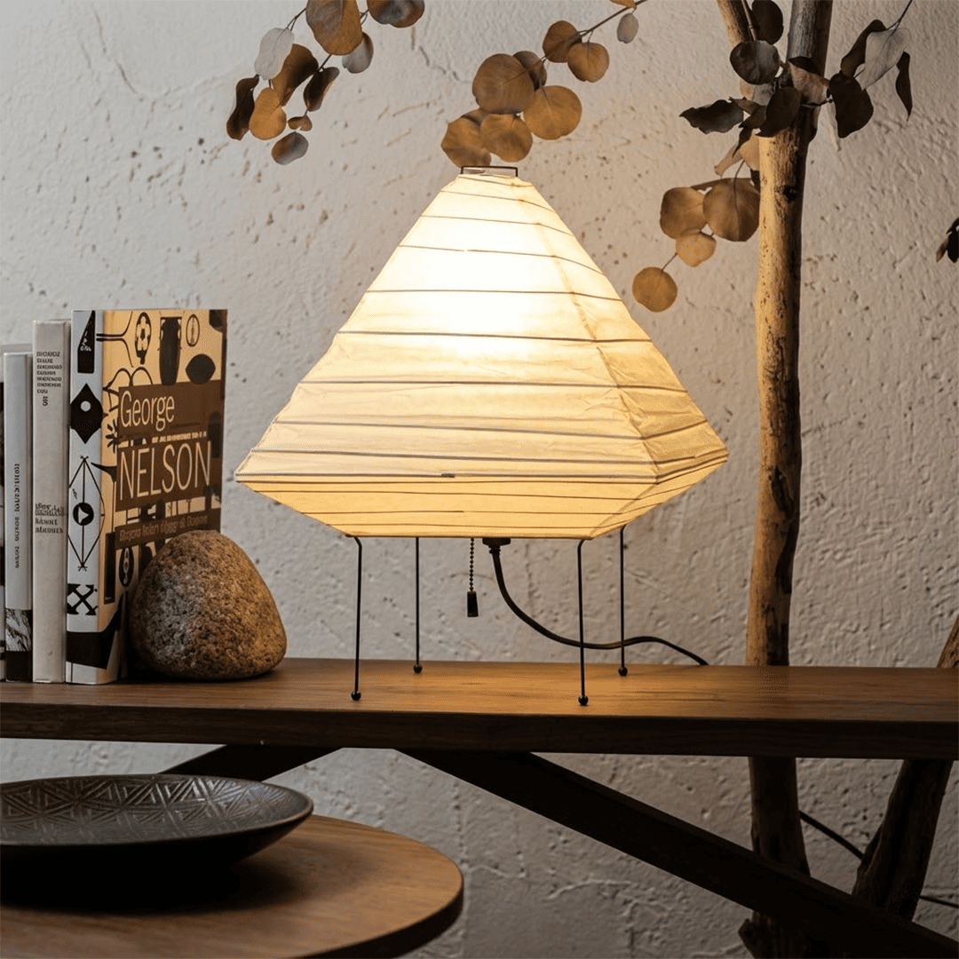 Minimalist modern home lamp: A geometric diamond-shaped washi paper table lamp with a tripod base, emitting a warm glow for cozy interior decoration lighting on a wooden desk.