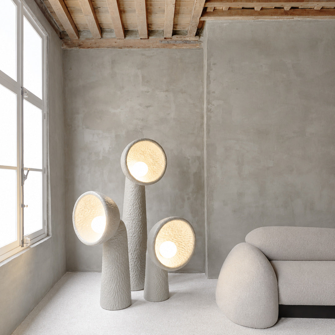 Totem sculptural floor lamp standing beside a sofa as a soft sculptural accent in a living room