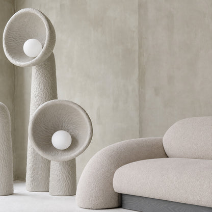 Totem sculptural floor lamp standing beside a sofa as a soft sculptural accent in a living room