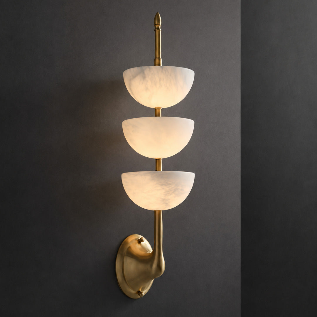 Warm integrated LED glow diffusing through the three alabaster tubes of the Trio wall sconce