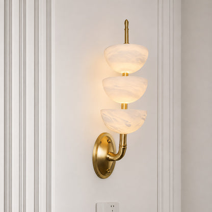 Warm integrated LED glow diffusing through the three alabaster tubes of the Trio wall sconce
