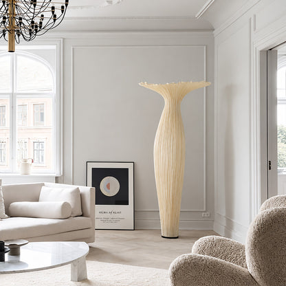 Vaso fabric floor lamp standing beside a sofa as a warm sculptural accent in a living room