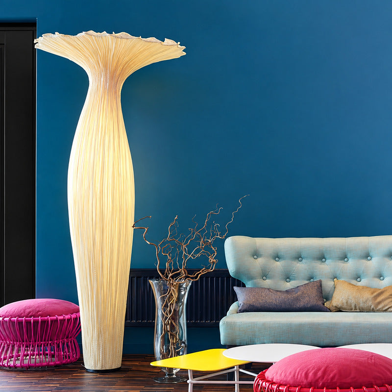 Vaso fabric floor lamp standing beside a sofa as a warm sculptural accent in a living room
