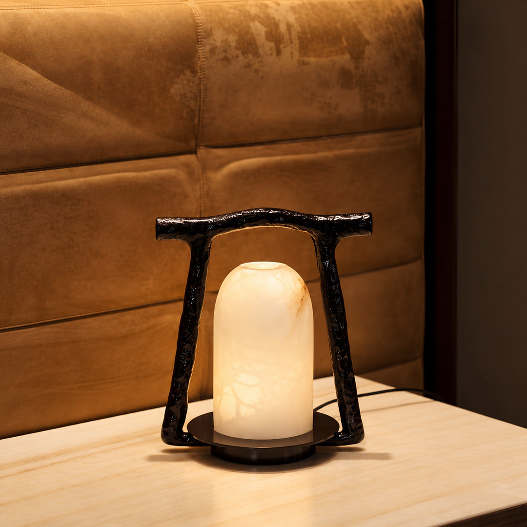 Volta alabaster table lamp casting a soft glow on a bedside table