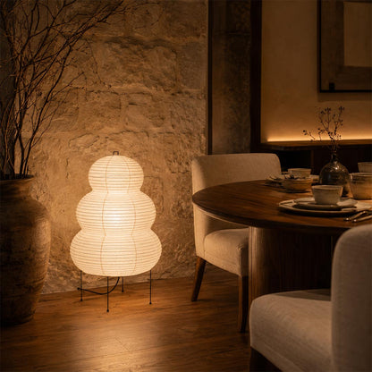 Moody dining space enhanced by a glowing Washi Paper 25N Floor Table Lamp against a textured plaster wall by Stuber Lighting.