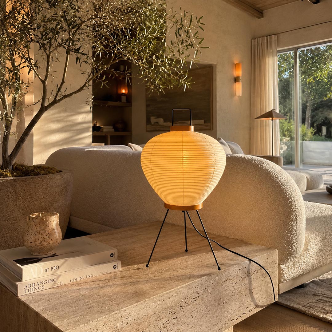 Washi Paper 3A Table Lamp with handle glowing warmly on a rustic wooden platform in a Japandi living room by Stuber Lighting.