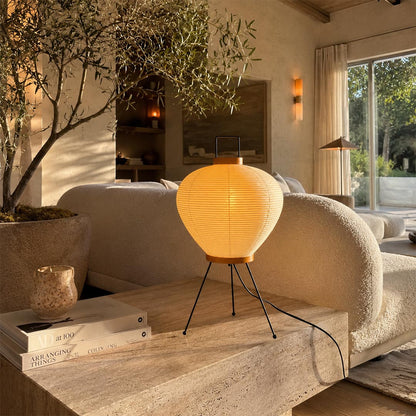 Washi Paper 3A Table Lamp with handle glowing warmly on a rustic wooden platform in a Japandi living room by Stuber Lighting.