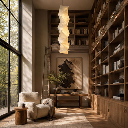 Dramatic Washi Paper L8 Pendant Light illuminating a cozy reading corner with a full-height wooden library bookshelf by Stuber Lighting.