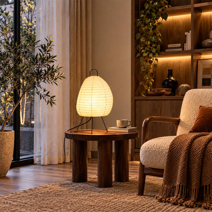Japanese style washi paper tall tripod table lamp set on a wooden side table in a cozy modern living room