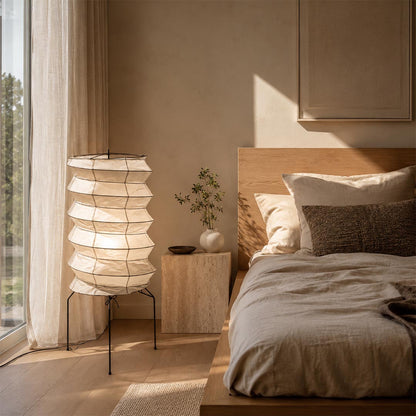 Relaxing bedroom atmosphere created by a tall layered Washi Paper UF2-31N Table Lamp beside a wooden platform bed by Stuber Lighting.