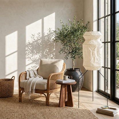 A sunlit reading nook featuring a Washi Paper UF3-L6 Tripod Lamp next to an armchair by an open window by Stuber Lighting.
